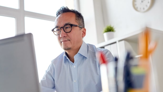 Person in blue button-down and glasses works in an office on a desktop computer.